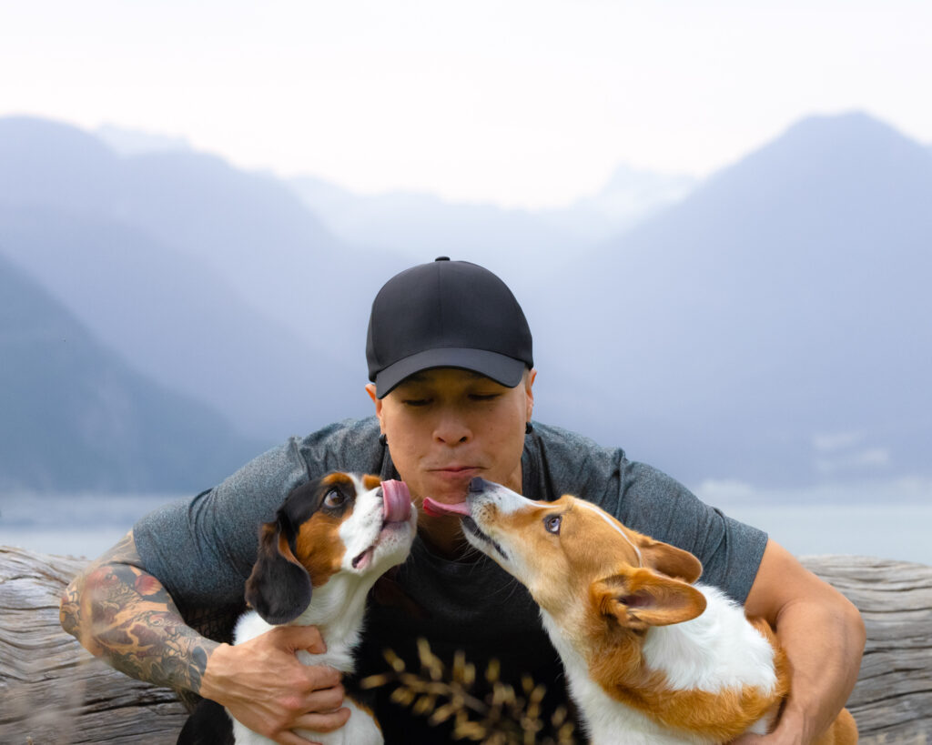 Two dogs giving their person kisses with mountain backdrop Taken by dog photographer in British Columbia. 